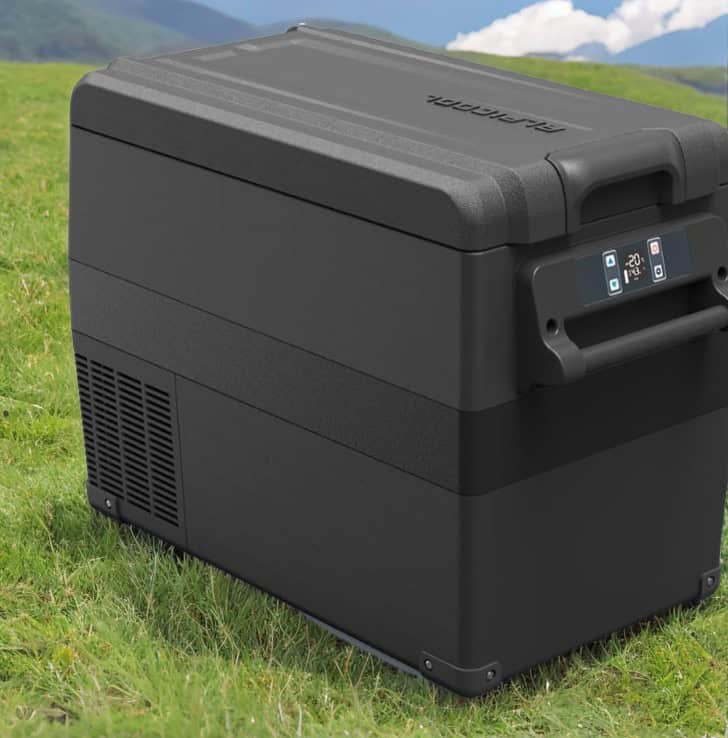 Alpicool NCF35 35L Kompressor Kühlbox in schwarz auf grüner Wiese mit Berglandschaft