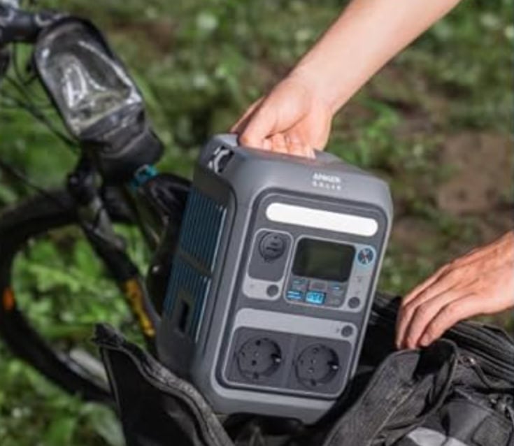Hand greift Anker SOLIX C300 Powerstation aus Rucksack mit Fahrrad im Hintergrund