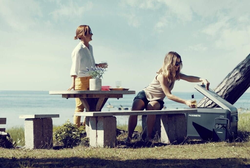 Zwei Frauen am Strand mit Dometic CFX3 Kühlbox auf Holzbank