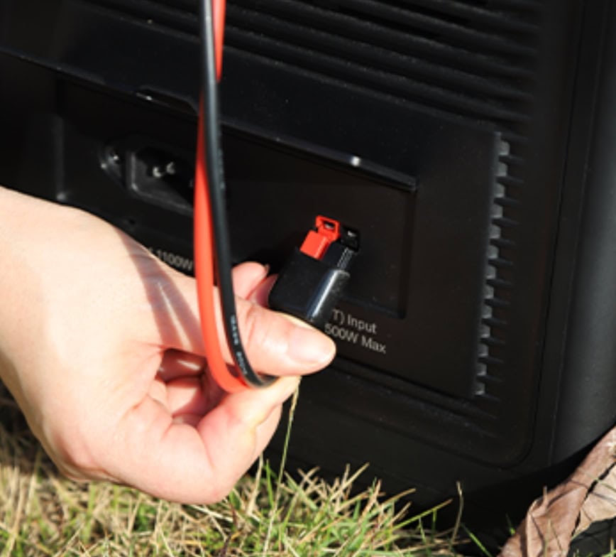 Hand steckt rotes Ladekabel in schwarze Powerstation ein